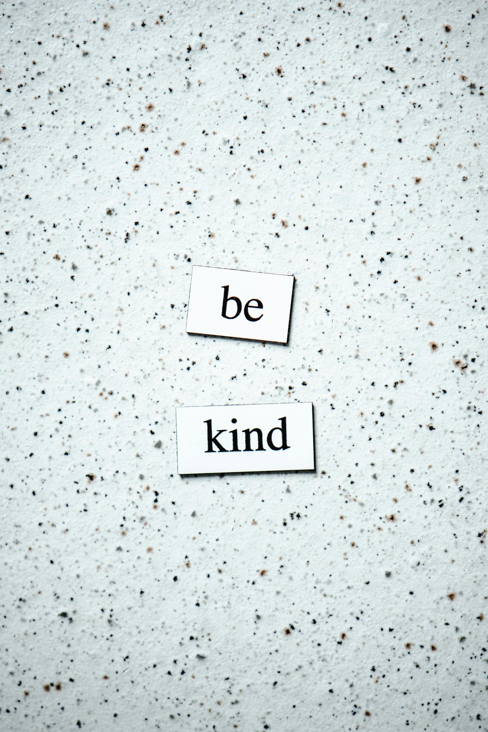 Inspirational 'Be Kind' message on a neutral speckled background, perfect for motivational themes.